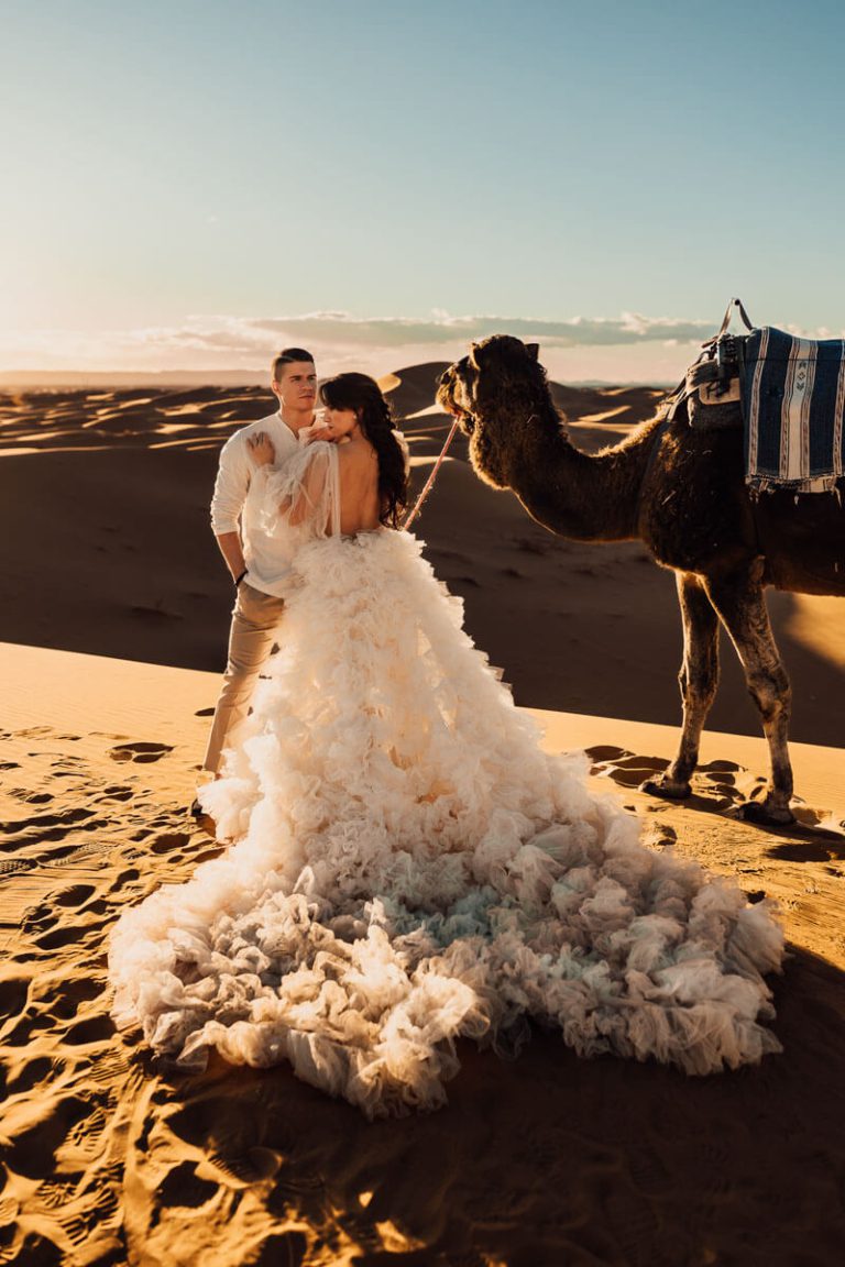 Hochzeitsshooting mit Kamel und ausladendem Kleid in der Wüste im Hochzeitsfotografie Bootcamp Marokko